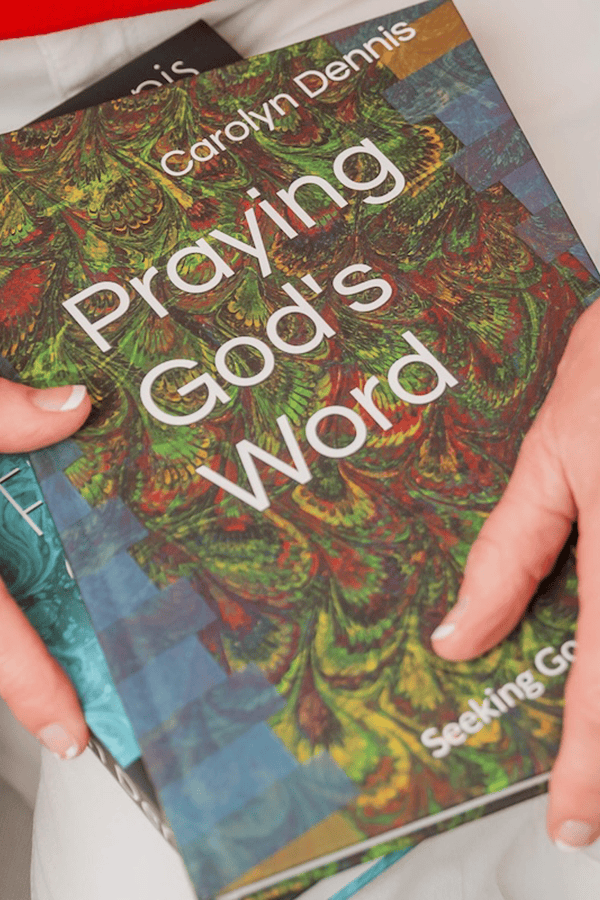 Close-up of Carolyn Dennis holding her book Praying God’s Word with a colorful patterned cover.